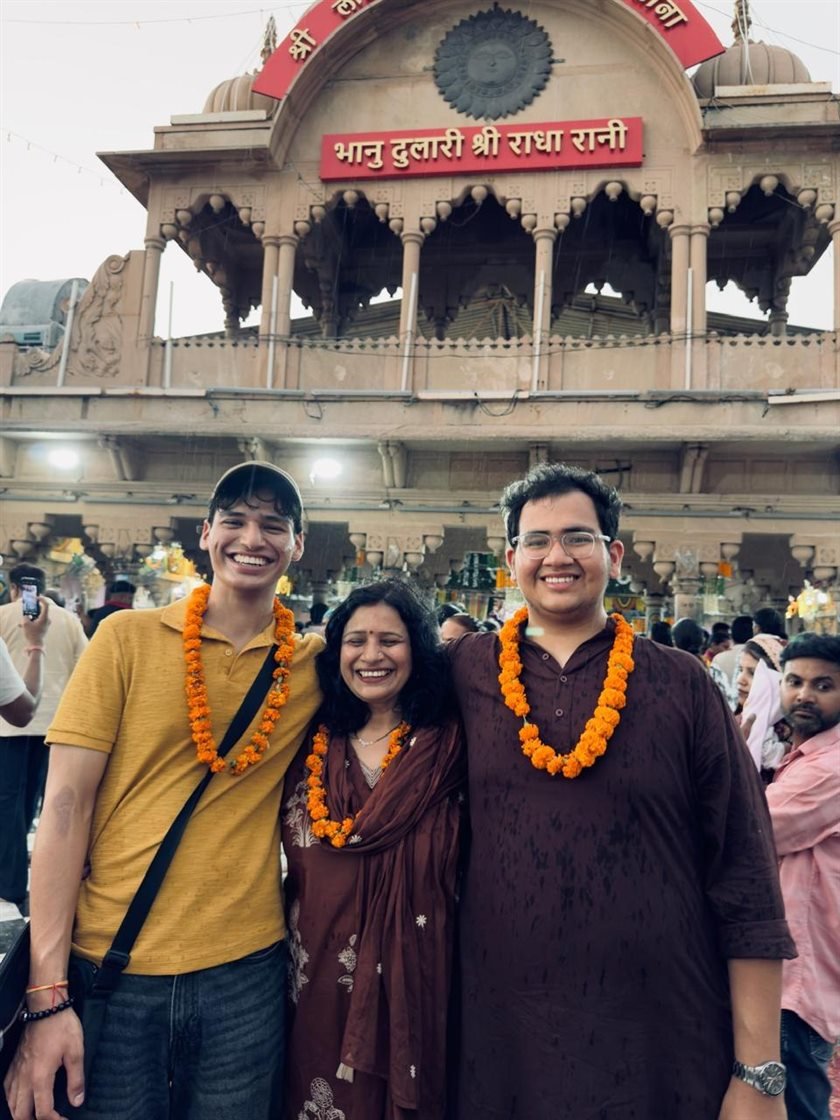 Three people wearing marigold garlands, smiling outside a temple